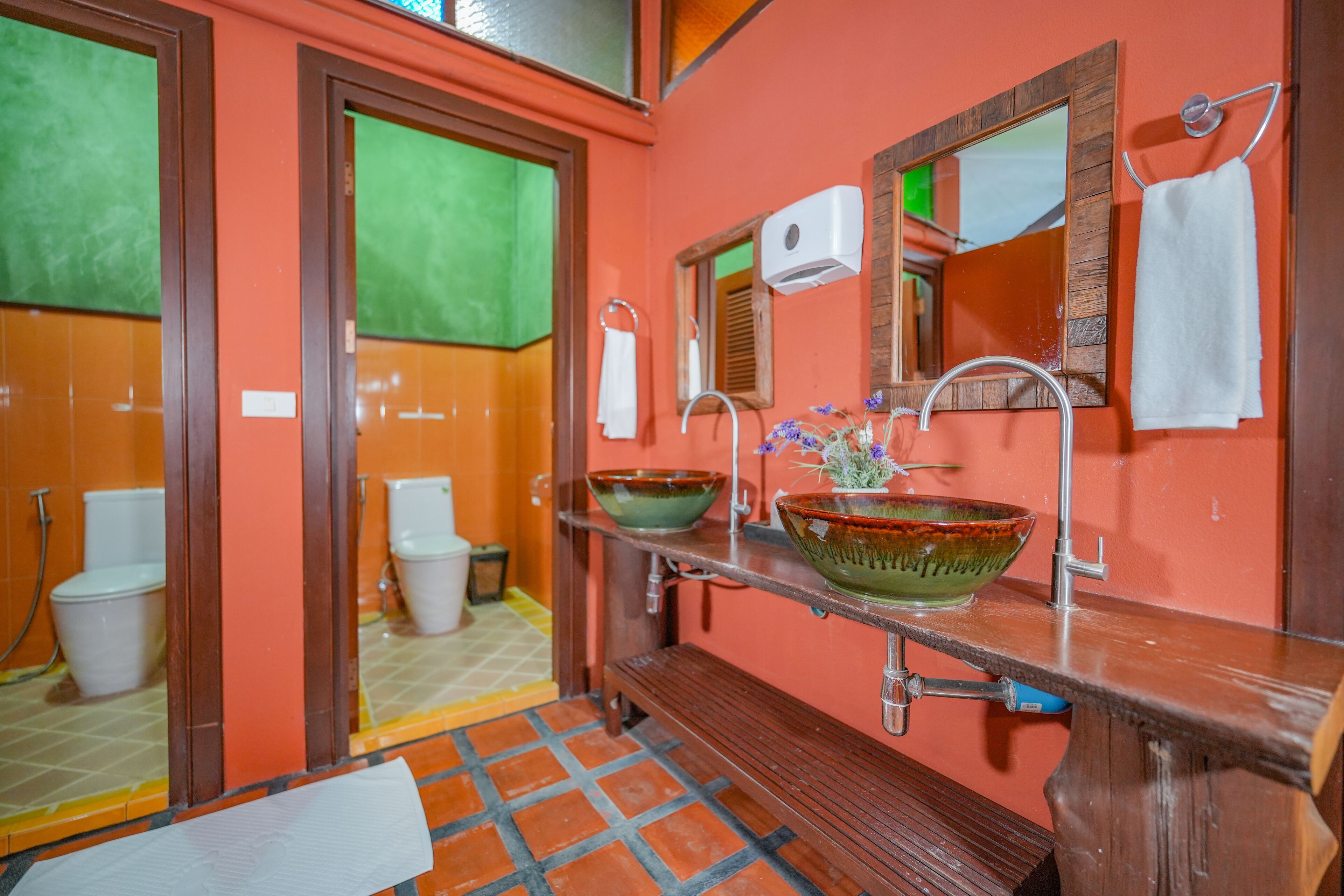 Un baño con un banco de madera, un lavamanos con un recipiente verde y un espejo con una toalla colgada.