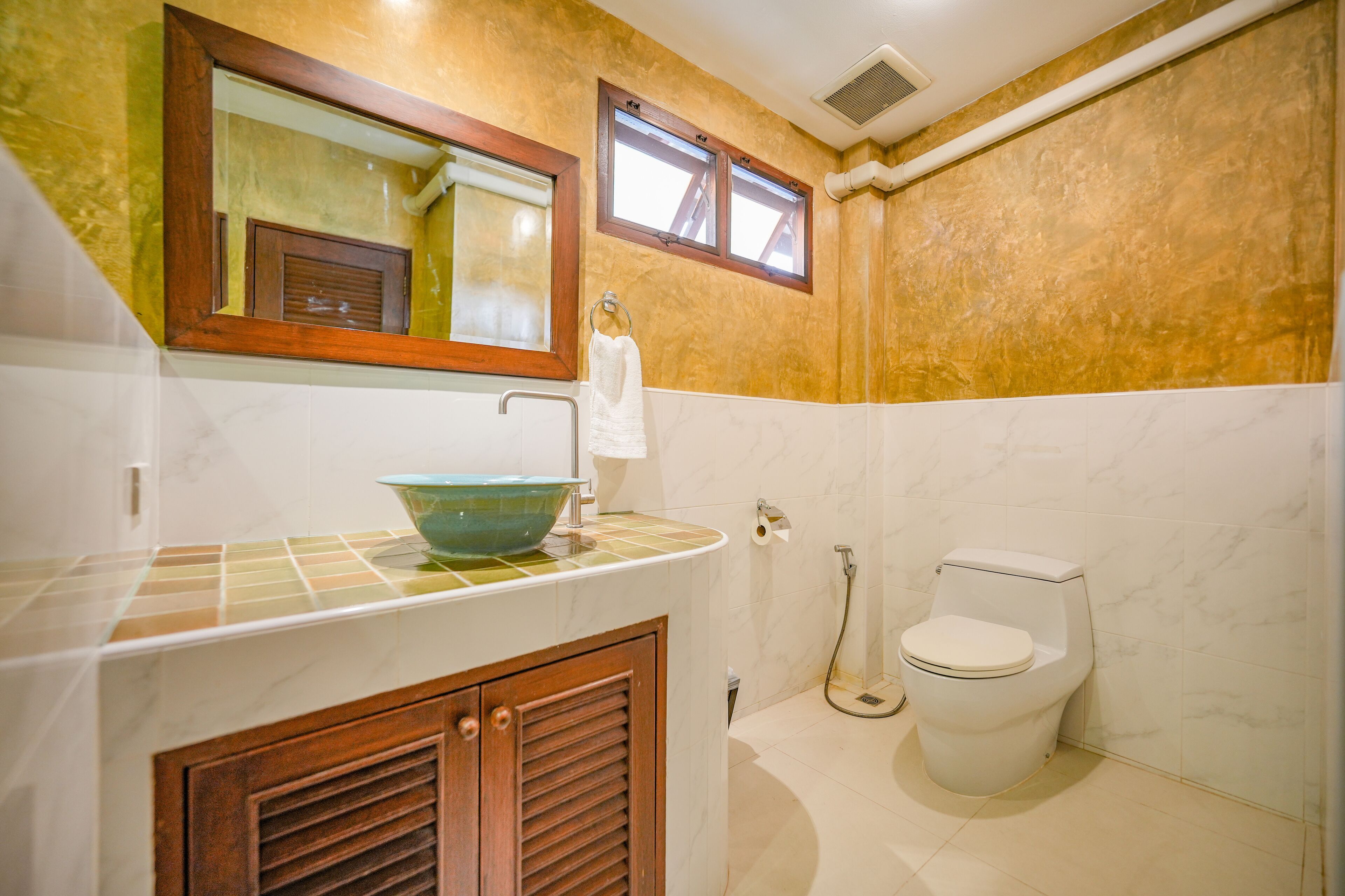 Un baño con lavamanos de mármol, inodoro, espejo y toallero.