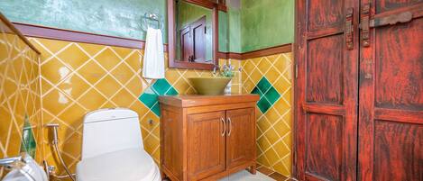 A bathroom with a toilet, sink, wooden cabinet, and a large wooden door.