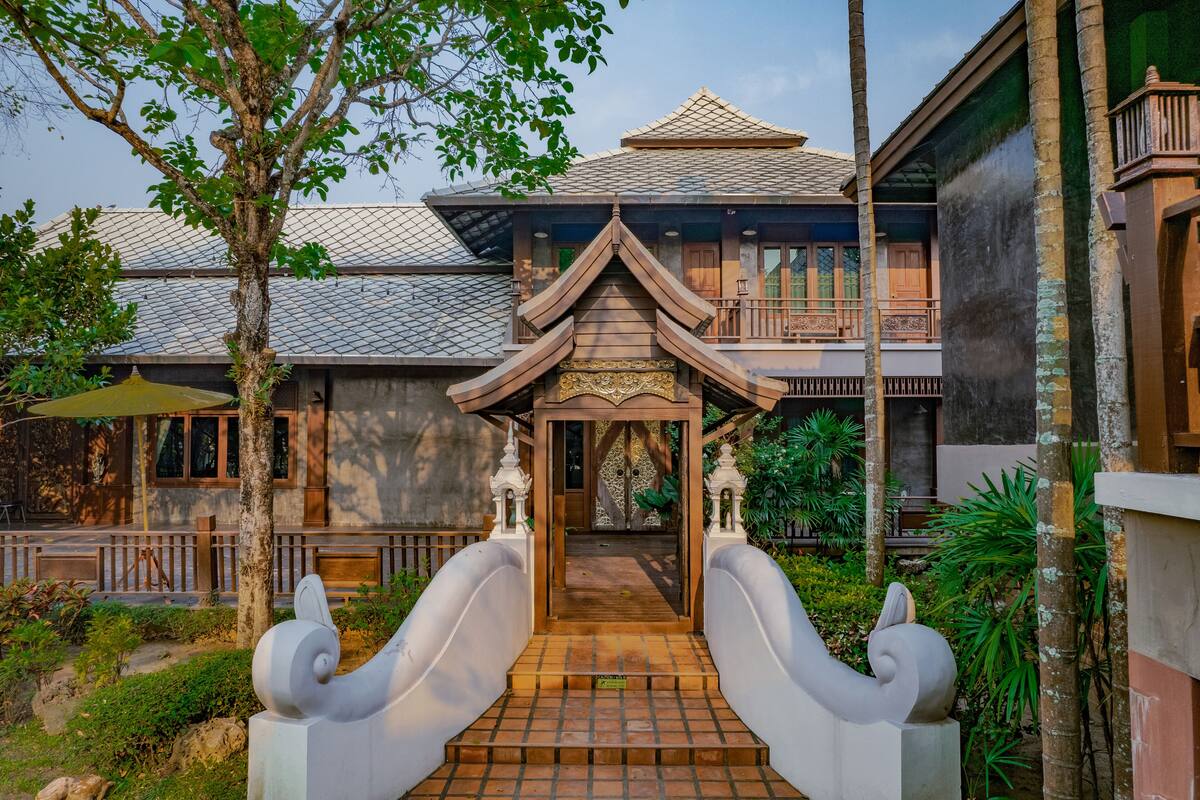 Un edificio tradicional con techo de tejas, un portón de madera y un pequeño jardín con un árbol y plantas.