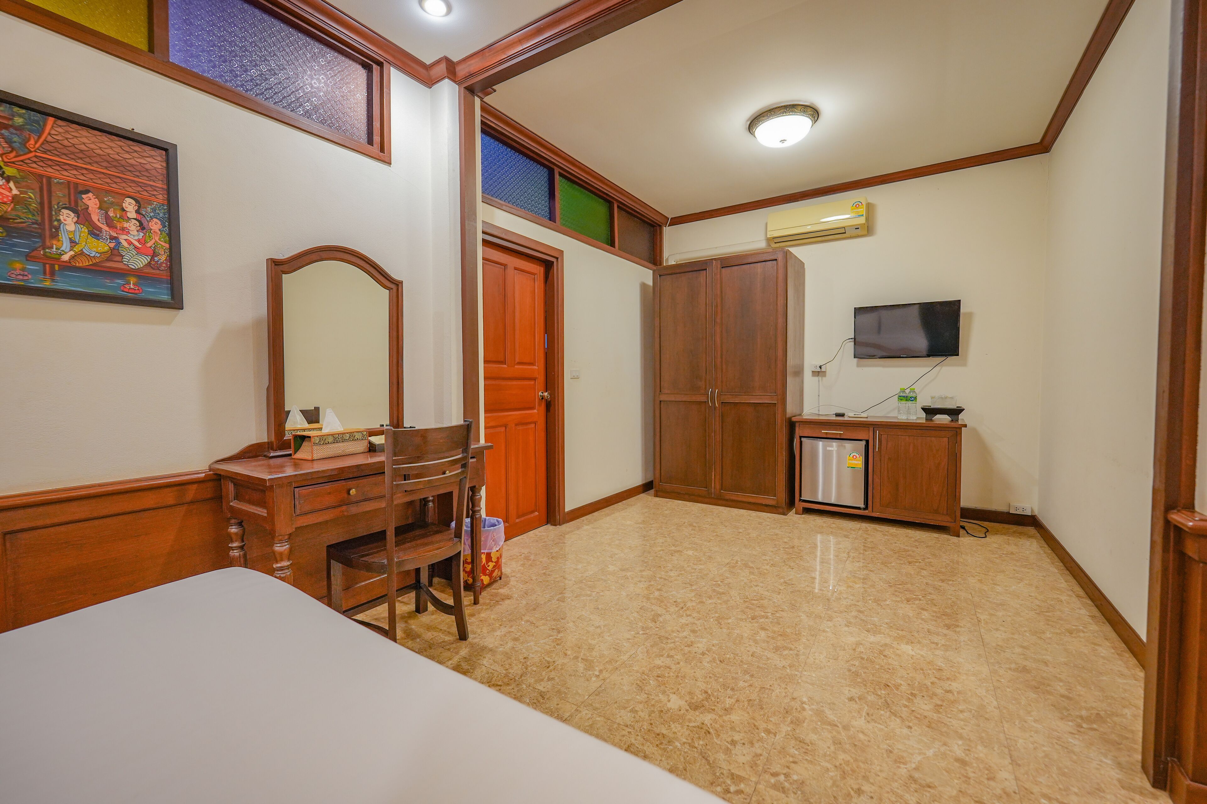 A bedroom with a bed, wooden dresser, mirror, wardrobe, and a television.