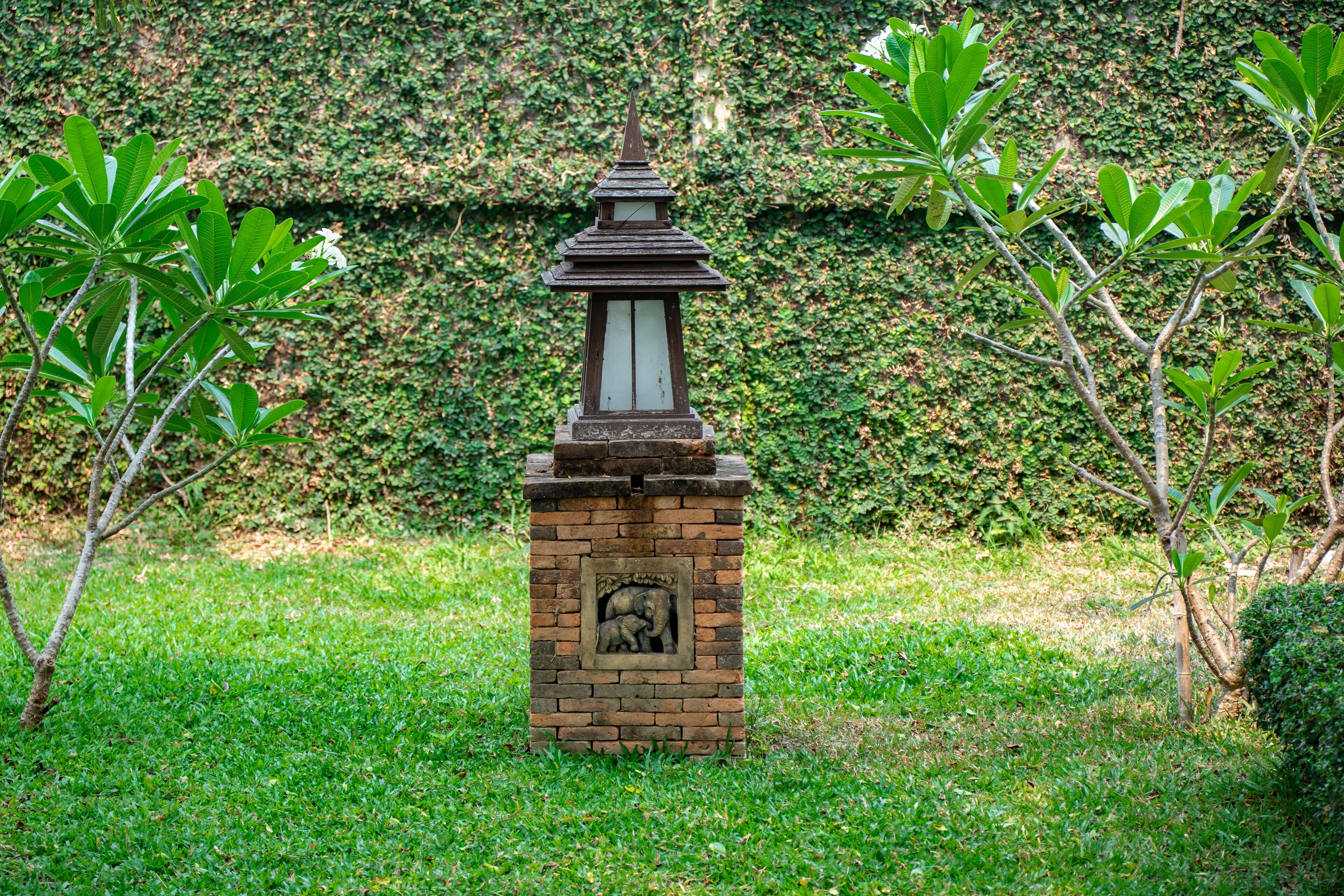 Un farol de ladrillo con diseño tradicional, situado en una zona con césped y follaje circundante.