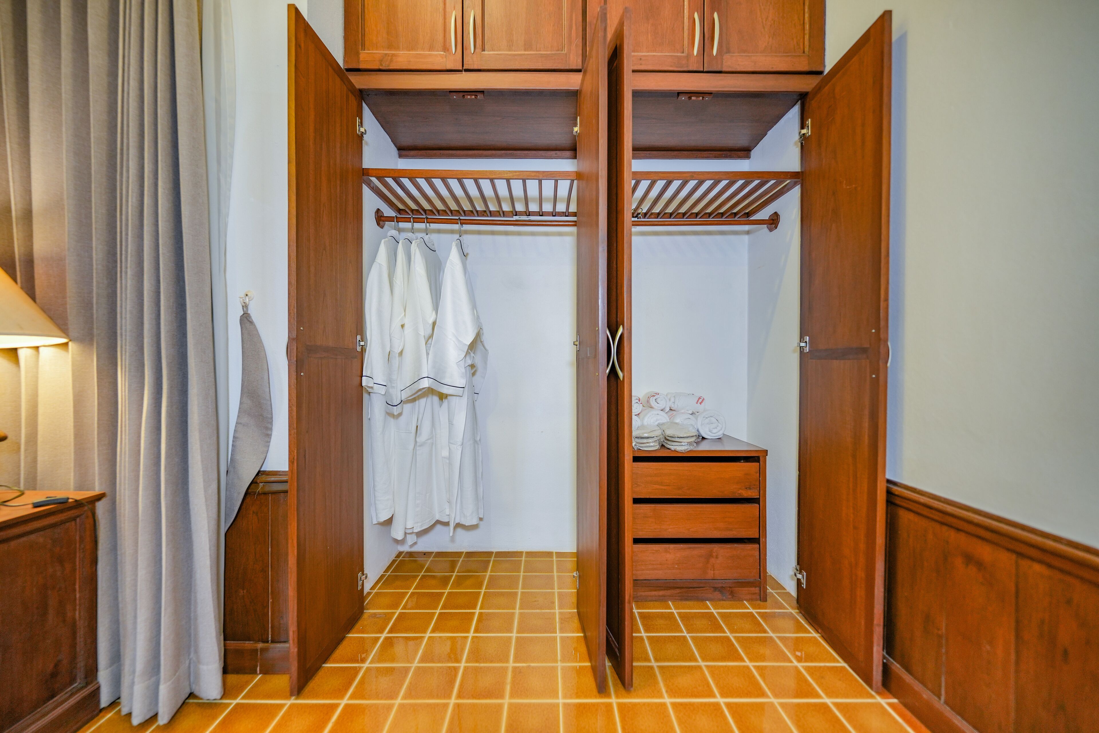 A walk-in closet with wooden doors, a hanging rack, and a shelf with folded clothes.