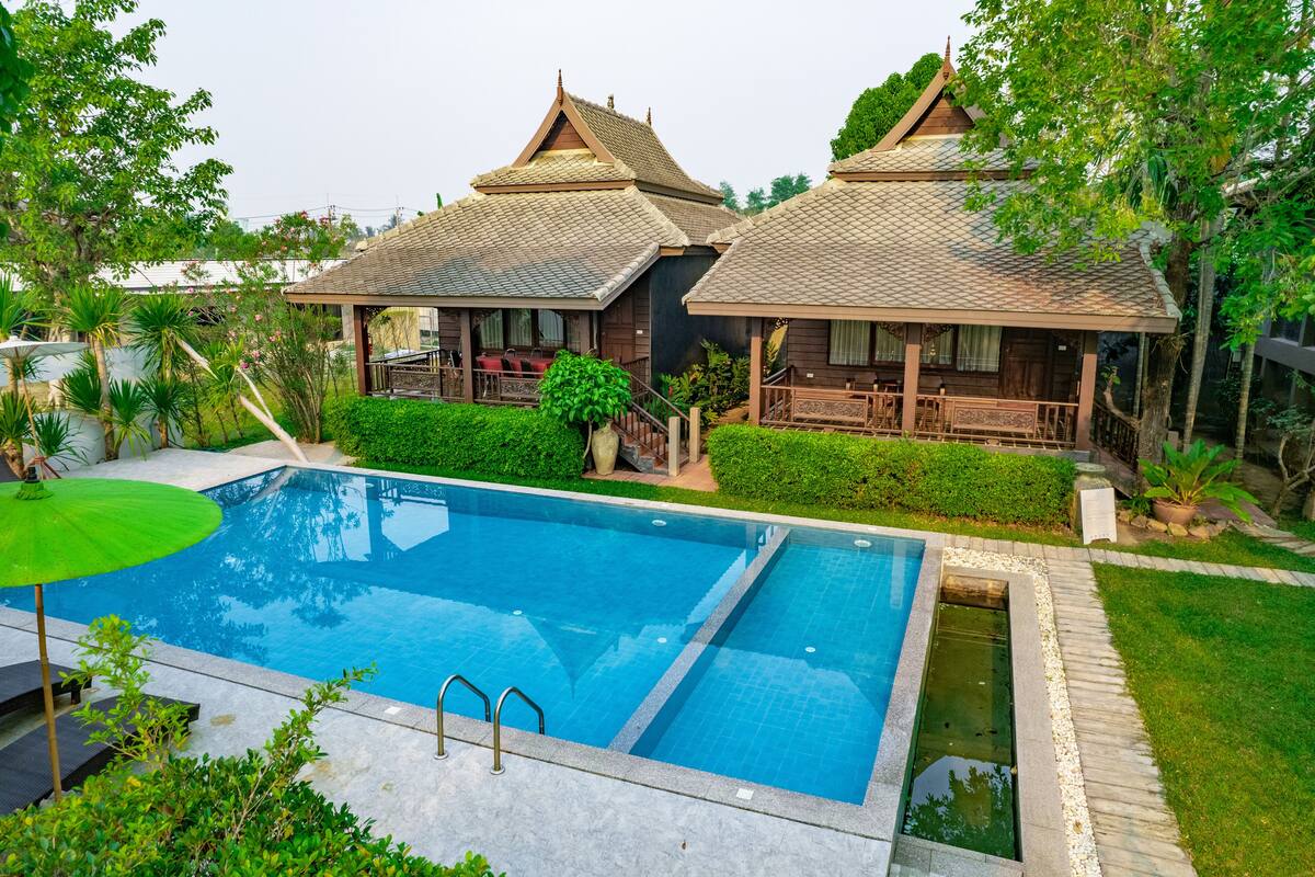 Un edificio de estilo tradicional con piscina, rodeado de follaje y un césped cuidado.