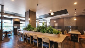 A modern restaurant with a long wooden bar, multiple seating areas, and a large window providing natural light.