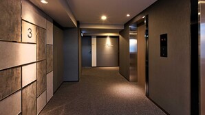 A hallway with a carpeted floor, a wall with numbered doors, and an elevator with a digital display.