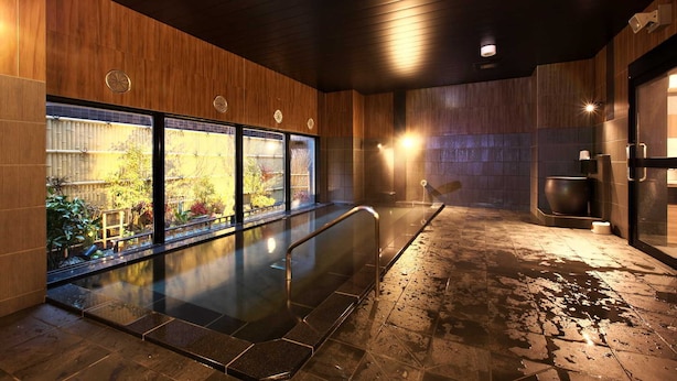 A modern indoor pool area with a glass wall, wooden paneling, and a stone floor.
