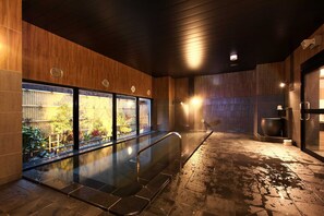 A modern indoor pool area with a glass wall, wooden paneling, and a stone floor. - Hotel Route Inn Grand Moriya Ekimae (Moriya)