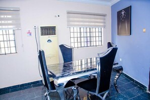 A room with a dining table and chairs, a window with bars, a door with a sign, and a framed picture on the wall. - Hill Crest Apartments (Ibadan)