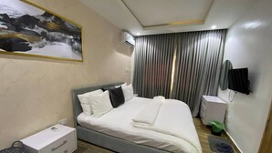 Quarto de hotel moderno com uma cama grande, mesa de cabeceira, escrivaninha e televisão montada.