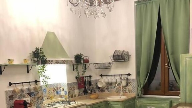 A kitchen with green cabinets, a gas stove, a sink, and a chandelier.