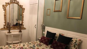 A bedroom with a floral bedspread, a mirror with an ornate frame, and a small bedside table.