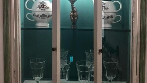 A glass display cabinet with a teal interior, containing white porcelain teapots and a candelabra.