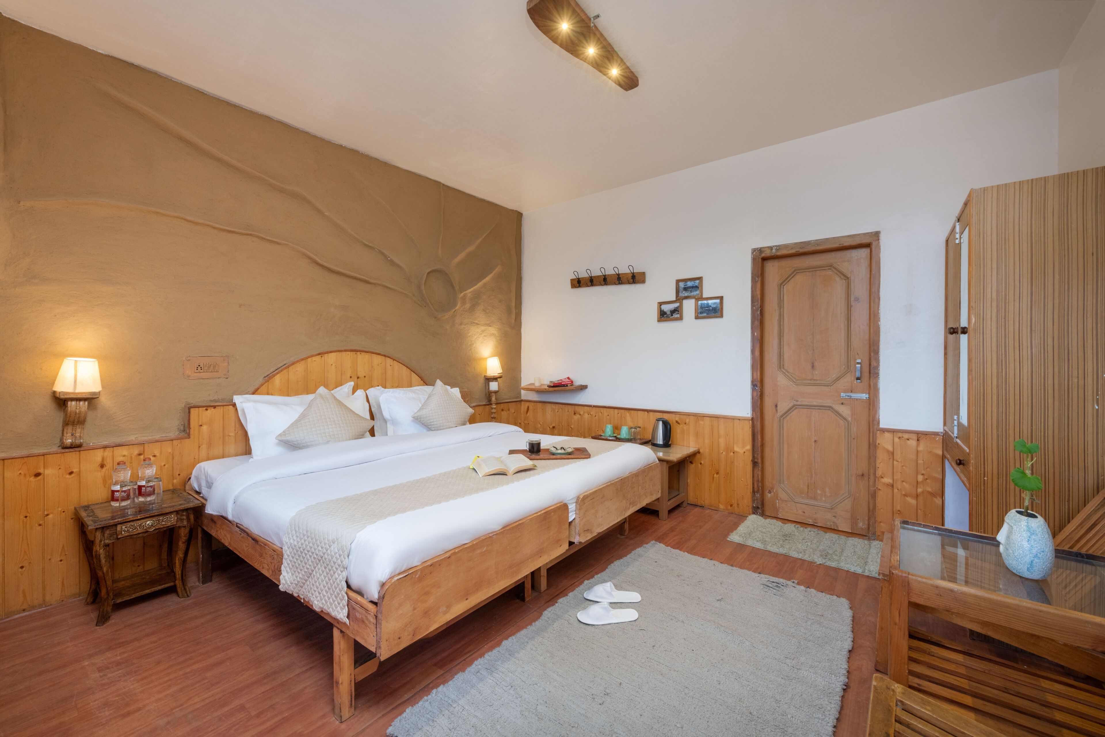 A bedroom with a wooden bed, bedside tables, a nightstand, a wooden wardrobe, and a wall-mounted shelf.