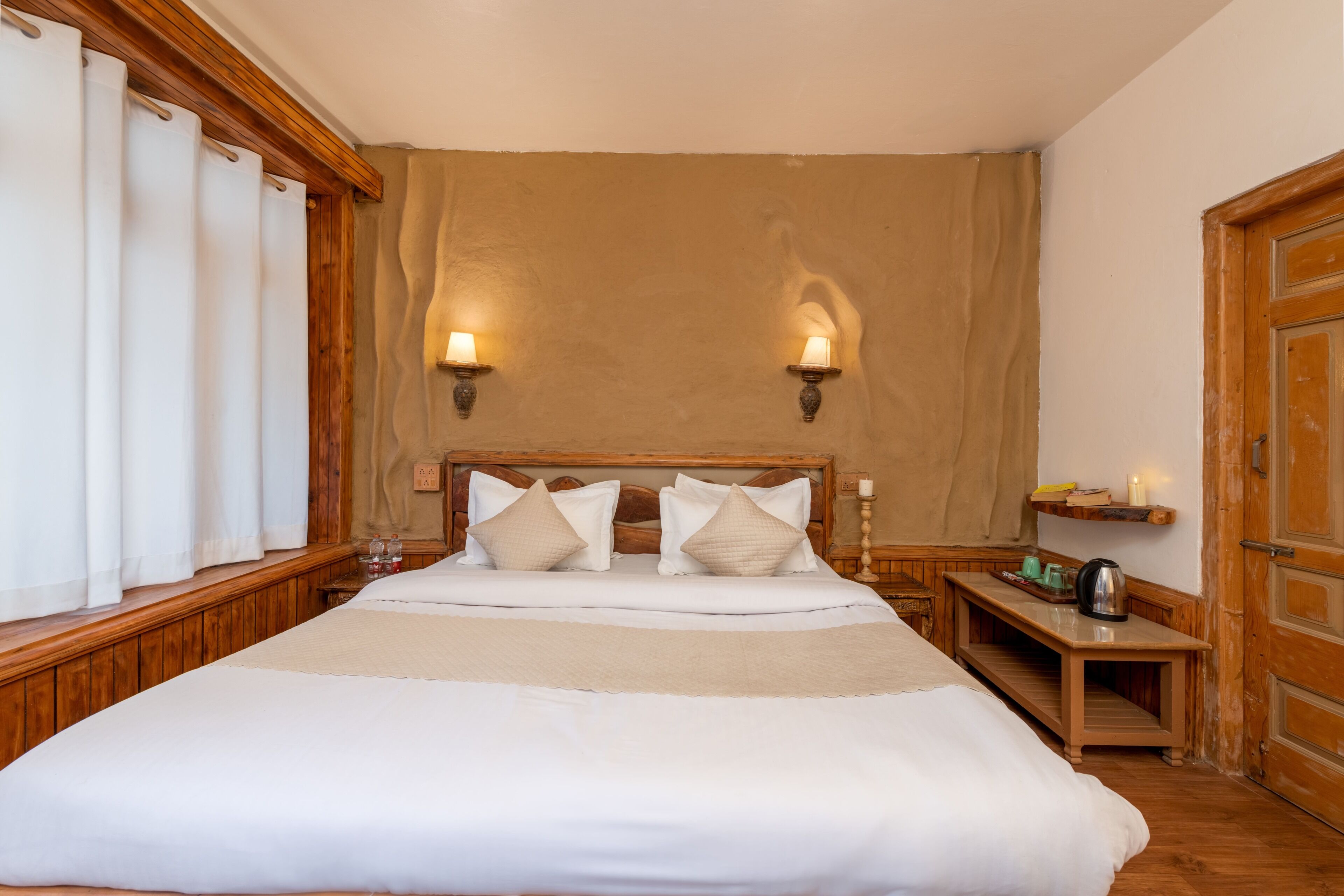 Ein Hotelzimmer mit einem großen Bett, zwei Wandlampen, einem Nachttisch aus Holz mit einer Kerze und einer Holztür.