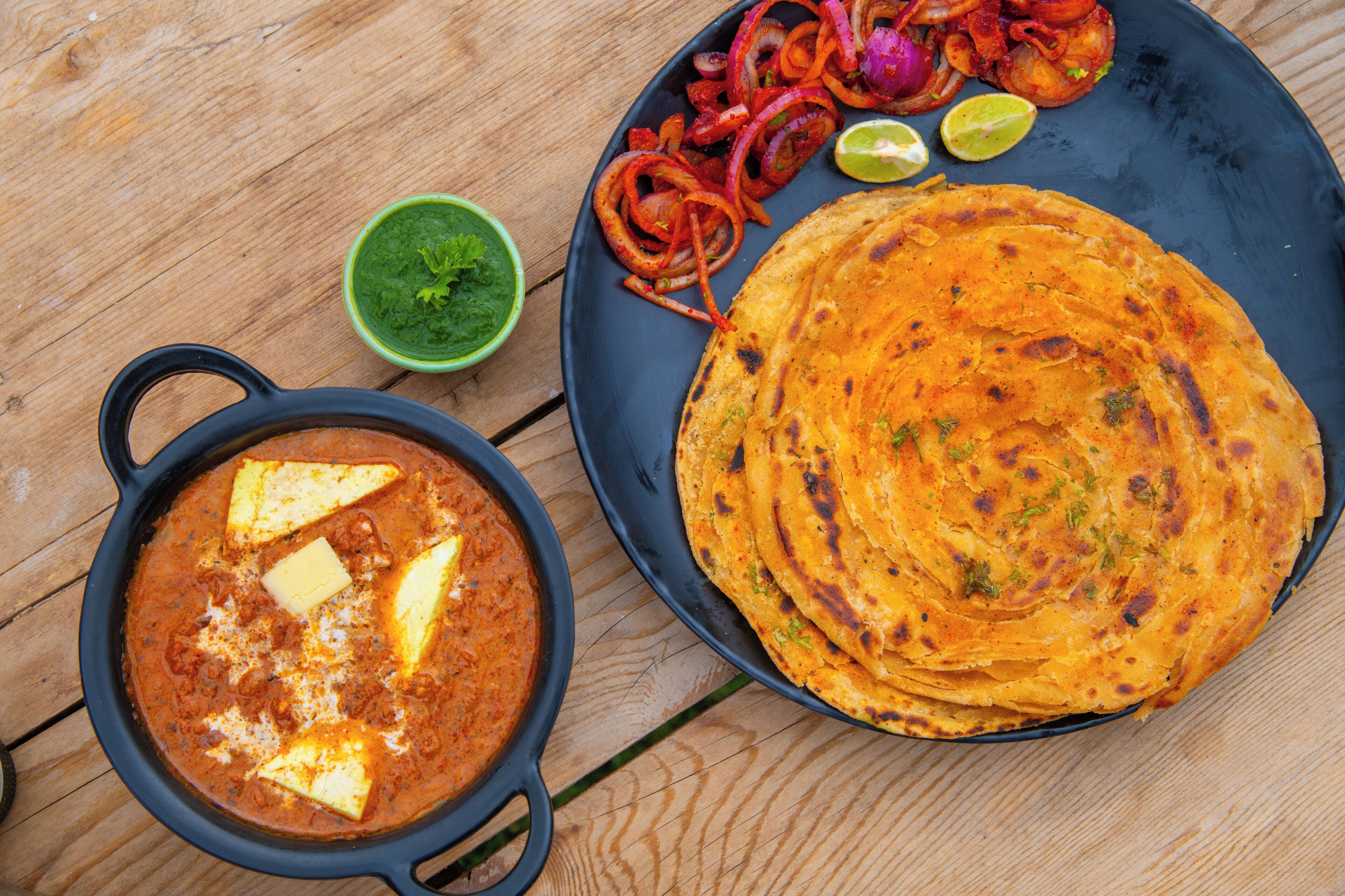 A meal with flatbreads, a bowl of curry, and a side of sliced onions.