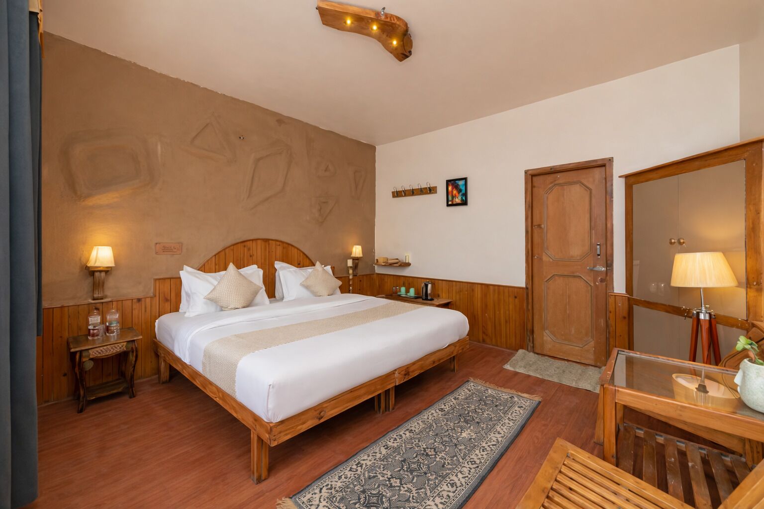 A bedroom with a wooden bed, bedside tables, a mirror, a door, and a small desk with a lamp.