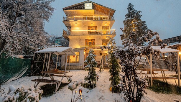 A multi-story hotel with balconies, a covered outdoor seating area, and snow-covered trees. - Beholden Stay & Cafe-Mountain View Boutique Stay in Old Manali (Manali)