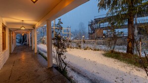 A covered outdoor area with a snow-covered path, a fence, and a building in the background. - Beholden Stay & Cafe-Mountain View Boutique Stay in Old Manali (Manali)