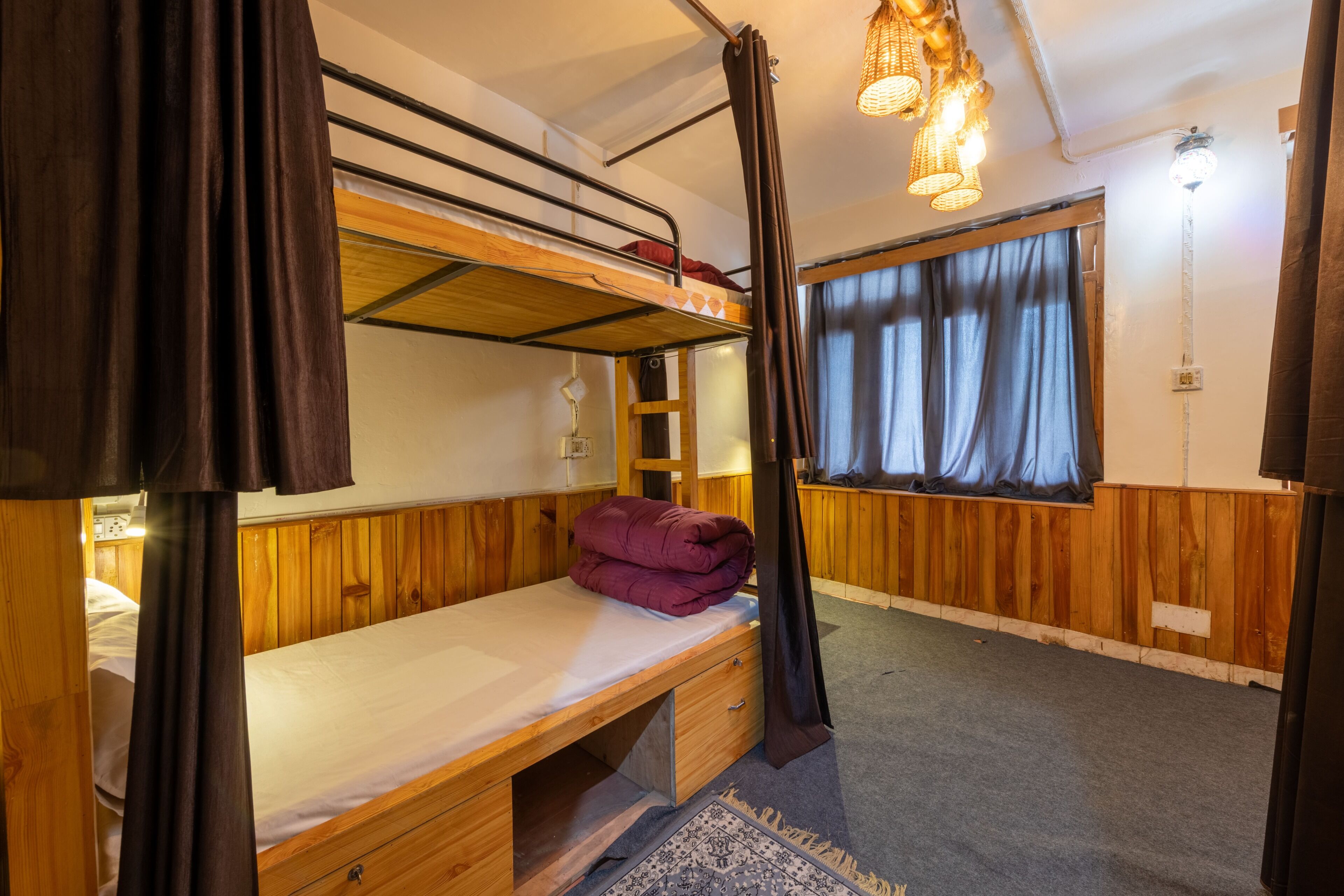 A bunk bed room with a wooden desk, a lamp, and a window with curtains.
