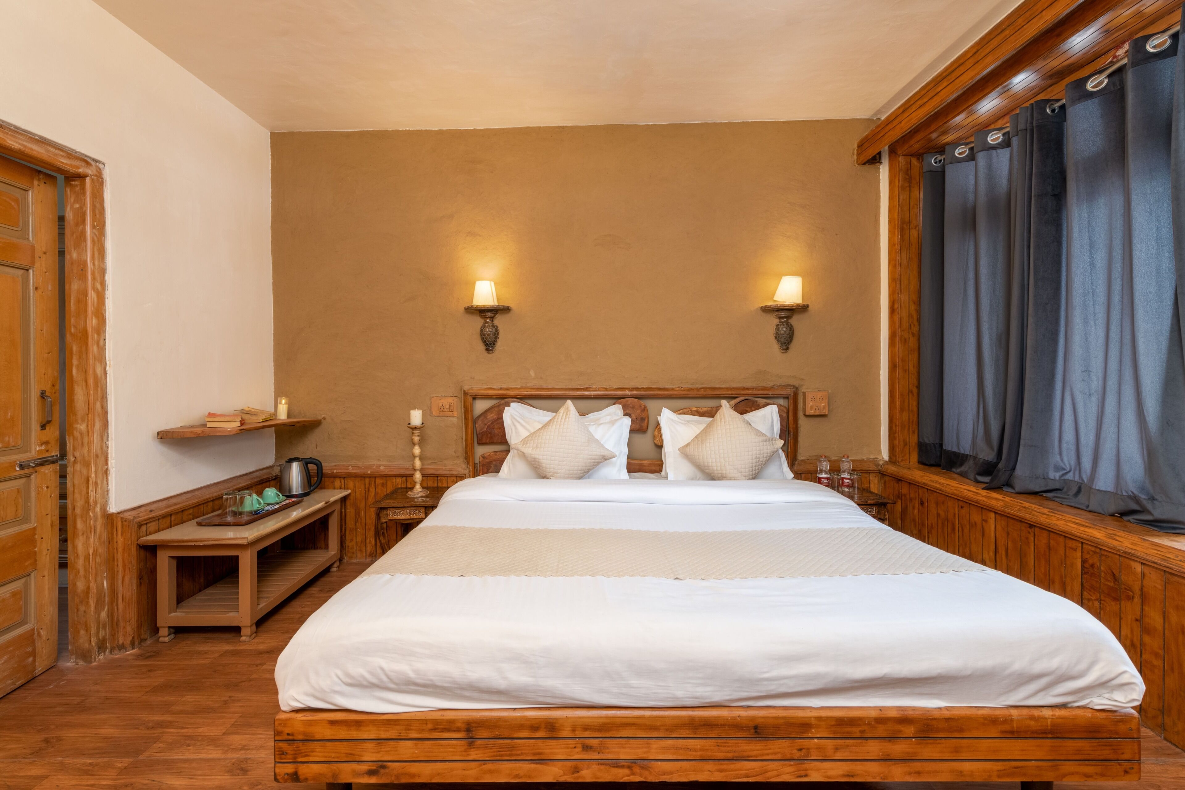 A hotel room with a wooden bed, two bedside lamps, a nightstand with a lamp, and a window with curtains.
