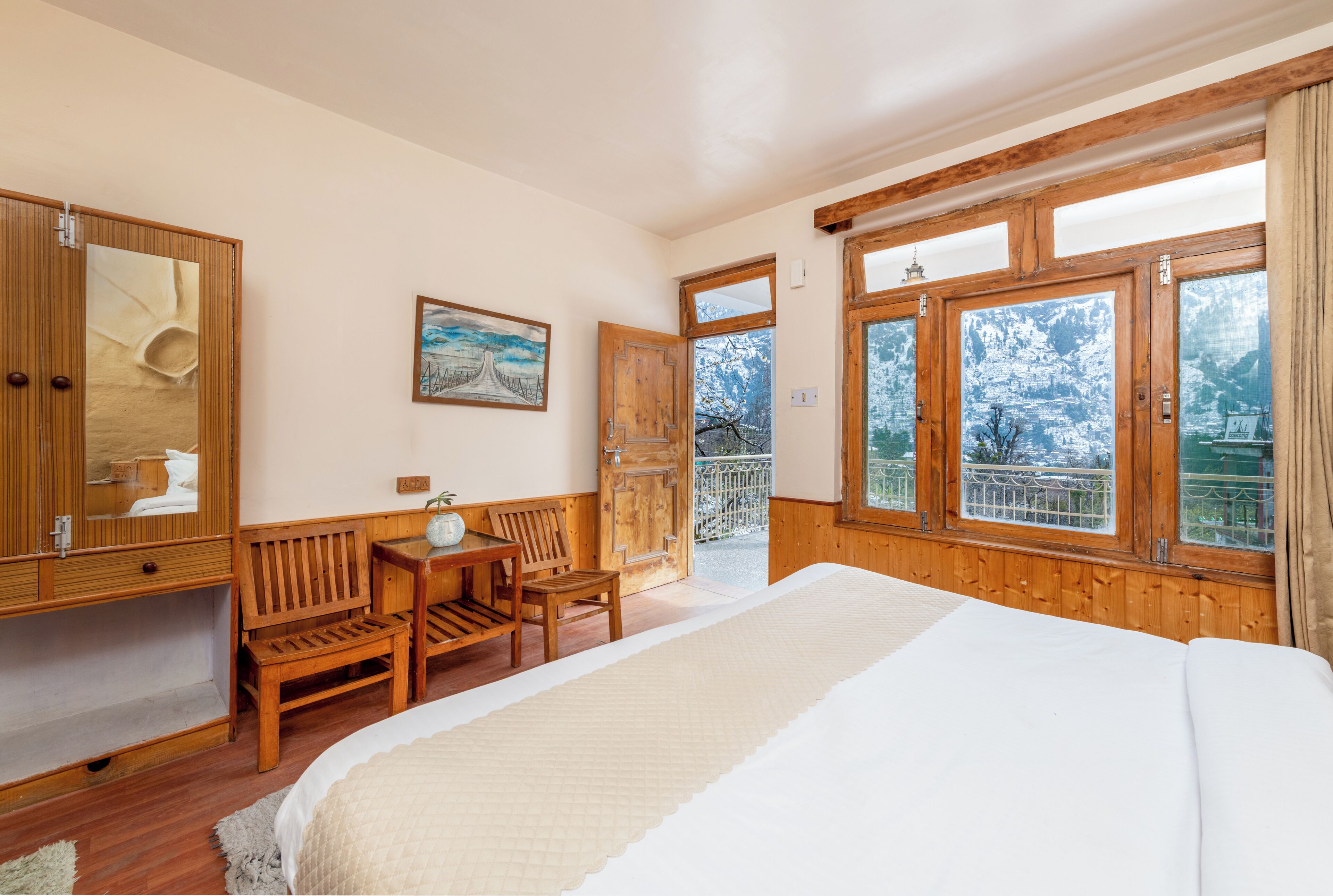A bedroom with a large bed, wooden furniture, a desk, and a view of a snowy landscape through large windows.