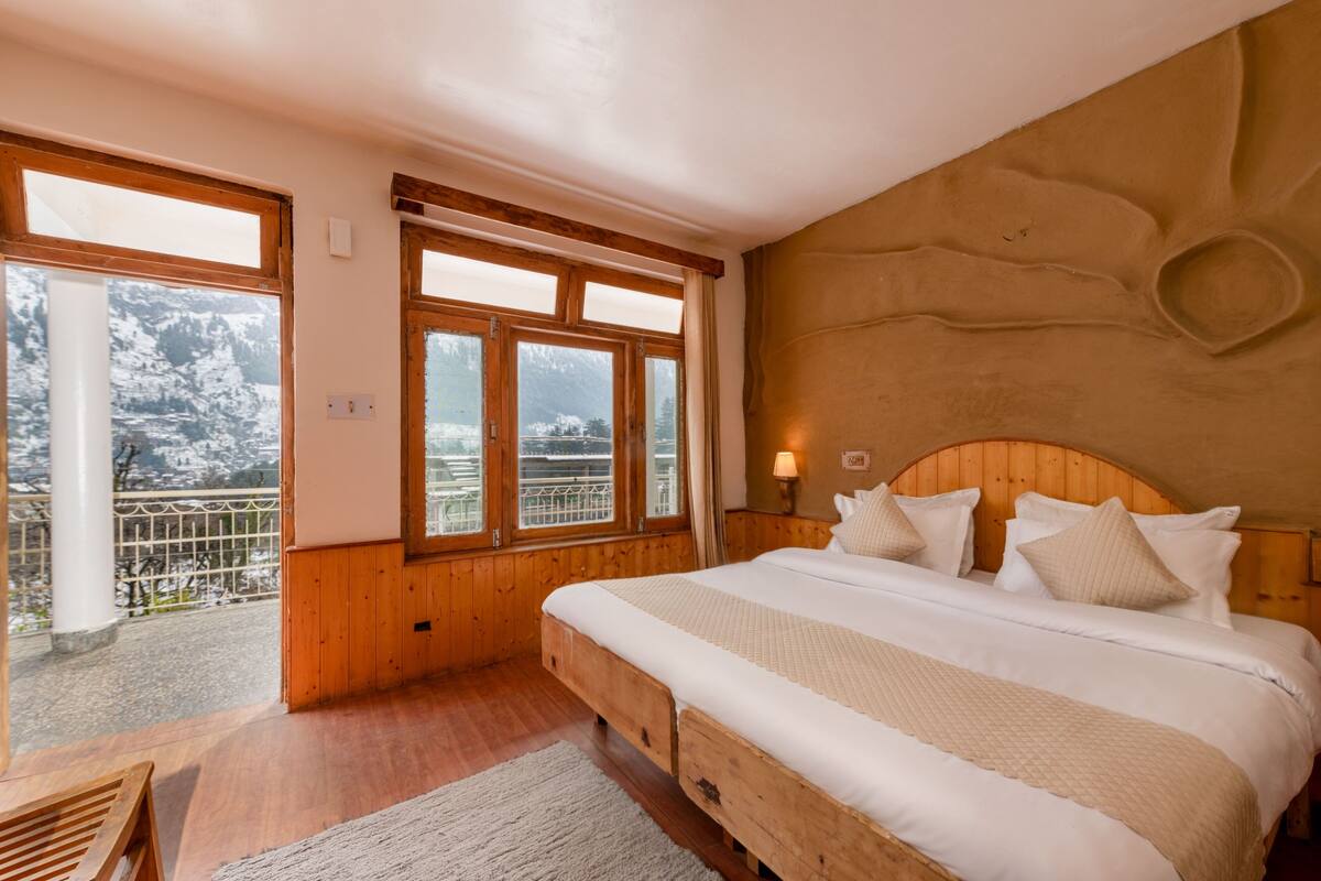Een slaapkamer met een houten bed, uitzicht op besneeuwde bergen en een balkon met een leuning.