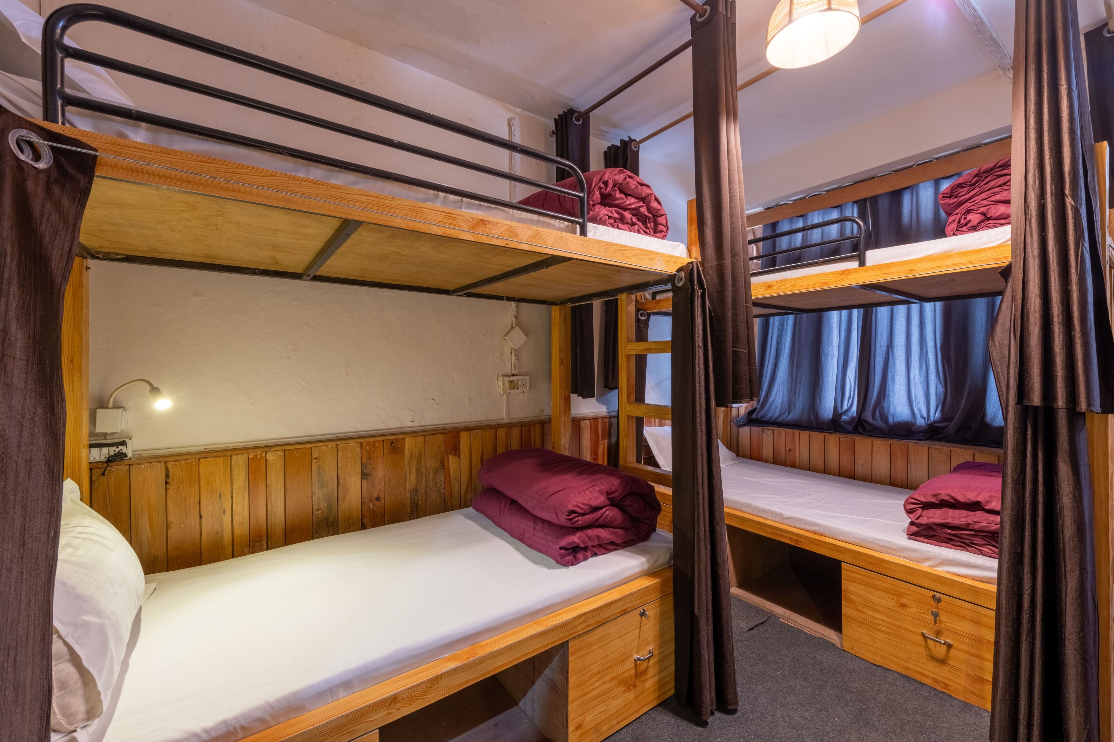 Habitación con literas, paredes de madera, un escritorio con cajón y una lámpara.