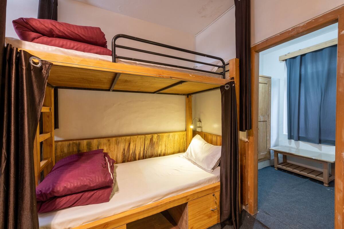 Een slaapkamer met een stapelbed, een houten hoofdbord, een nachtkastje en een bankje in de hoek.