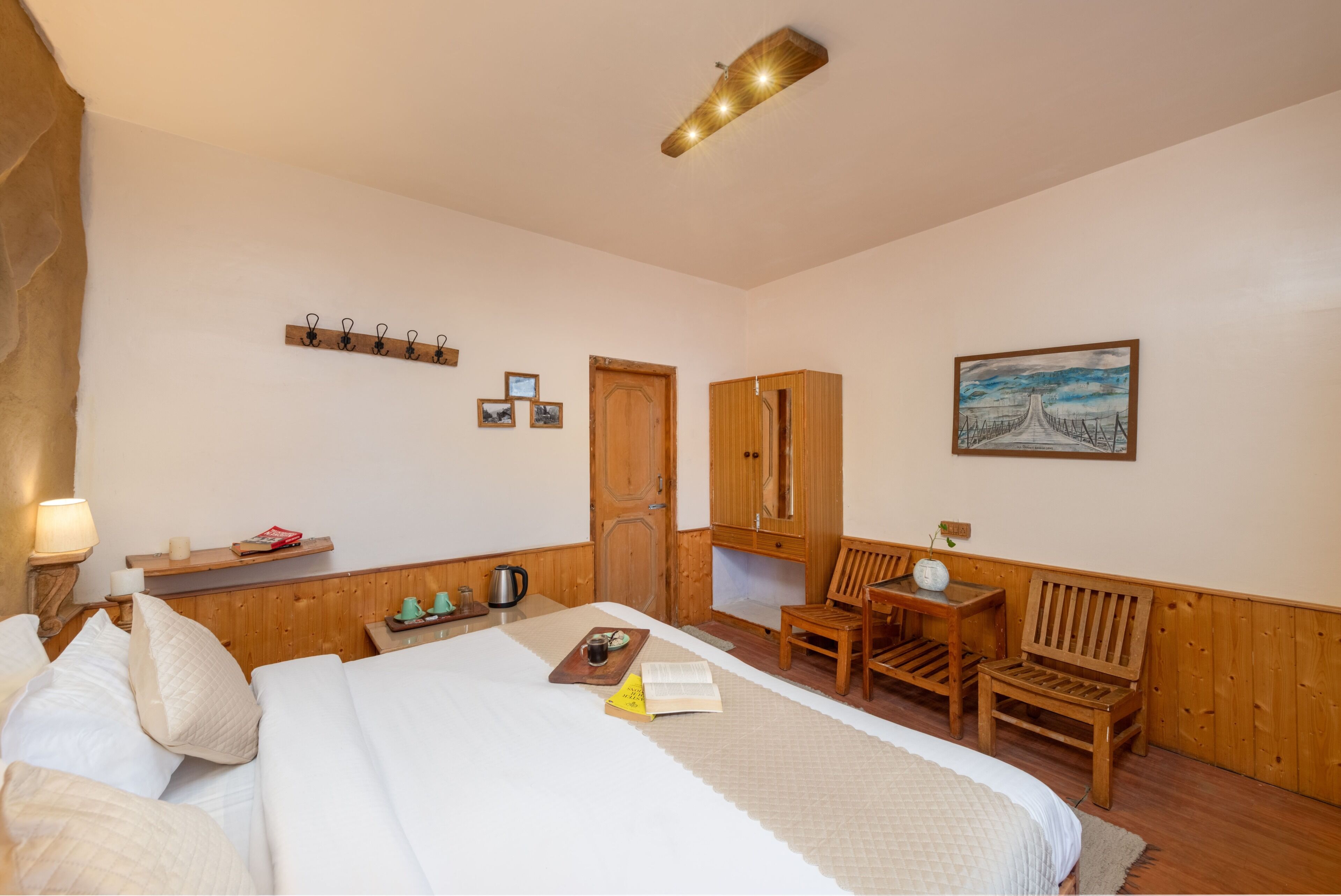 A bedroom with a bed, bedside table, lamp, wooden wardrobe, and a painting on the wall.