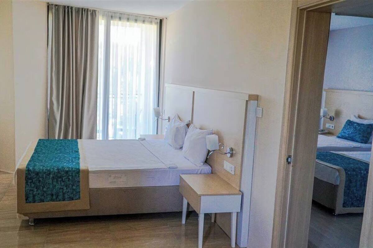 Habitación de hotel con cama, mesita de noche y vistas al exterior a través de una ventana con cortinas.