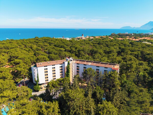 A multi-story hotel surrounded by dense greenery, with a view of the sea and distant mountains. - Pirates Park Resort -All Inclusive (Kemer)