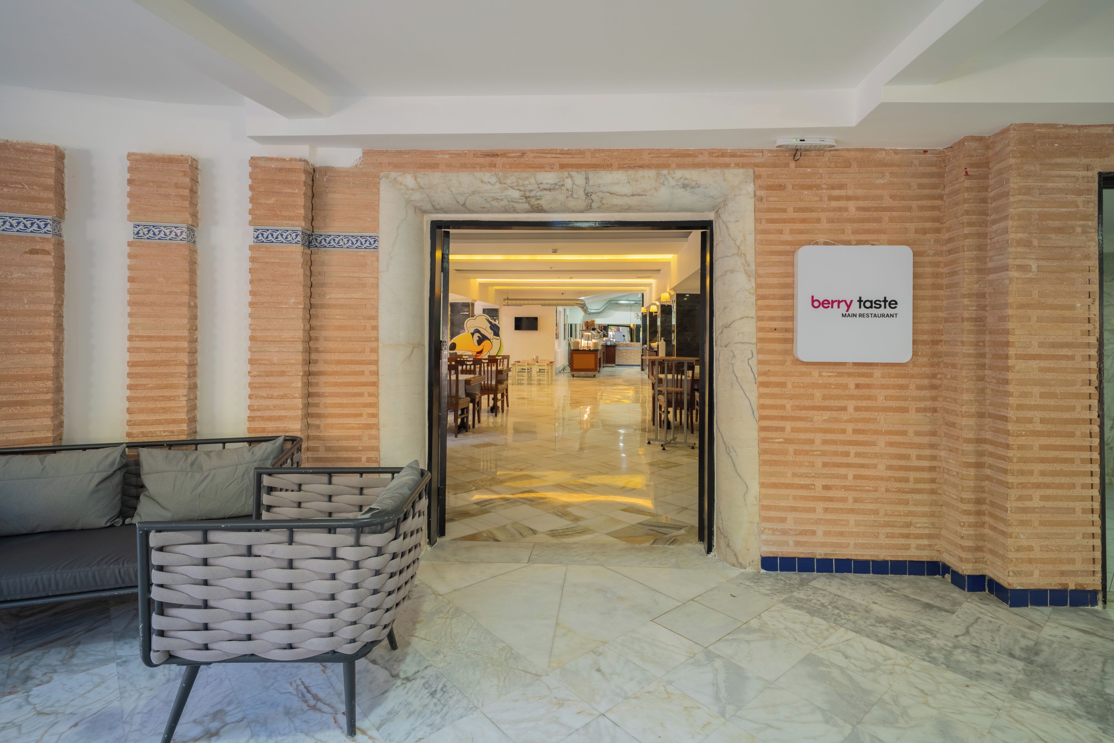 A lobby with a brick wall, a sign for 'berry taste main restaurant,' a sofa, and a chair.
