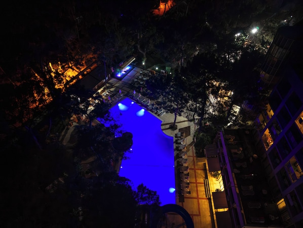 A nighttime view of a building with a blue-lit pool area, surrounded by trees and illuminated by streetlights.