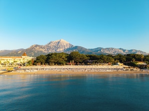 A coastal hotel with a view of mountains, a beach, and a pool area.