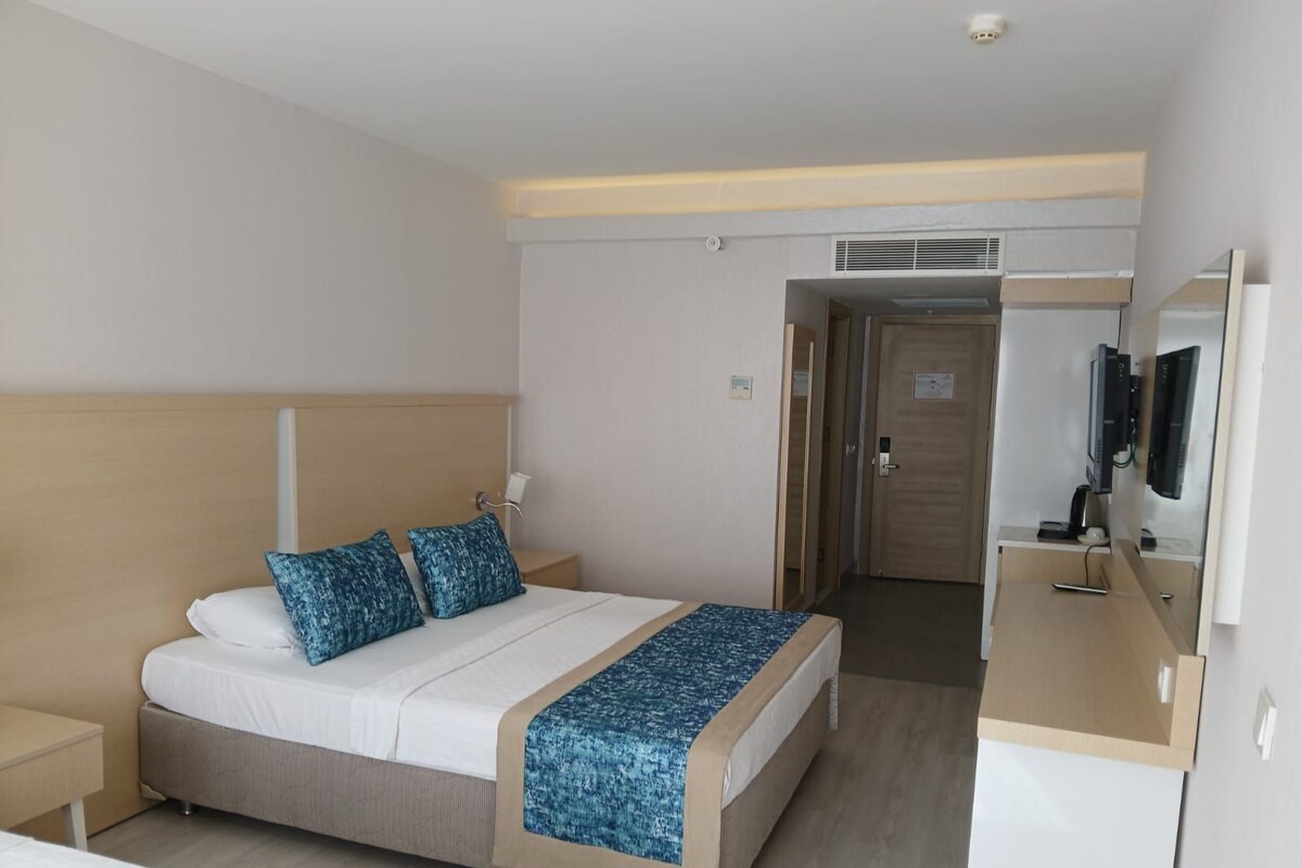 A hotel room with a bed, bedside table, and a desk with a computer.