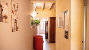 A narrow hallway with tiled flooring, a red trash bin, and various framed pictures on the walls. - Al Podestà (Mantua)