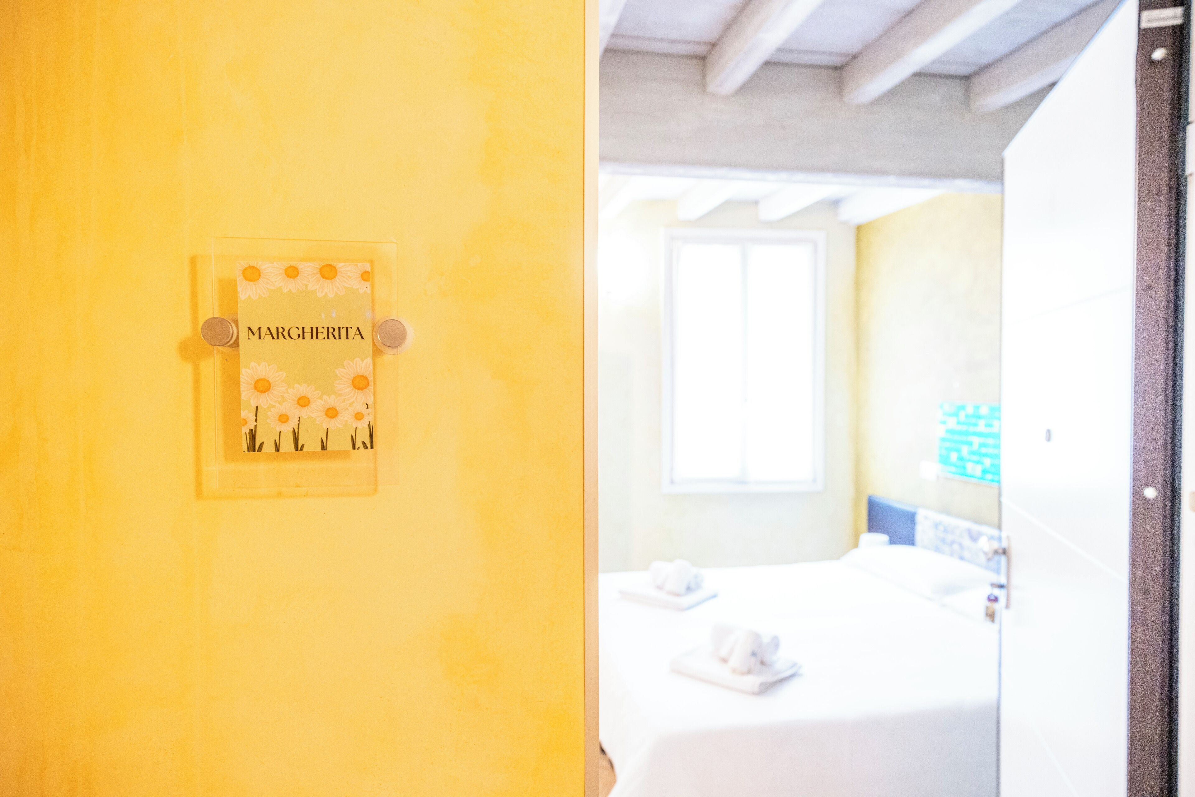 Quarto com cama, janela e placa na parede com o nome "MARGHERITA".