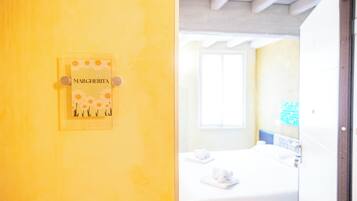 Quarto com cama, janela e placa na parede com o nome "MARGHERITA".