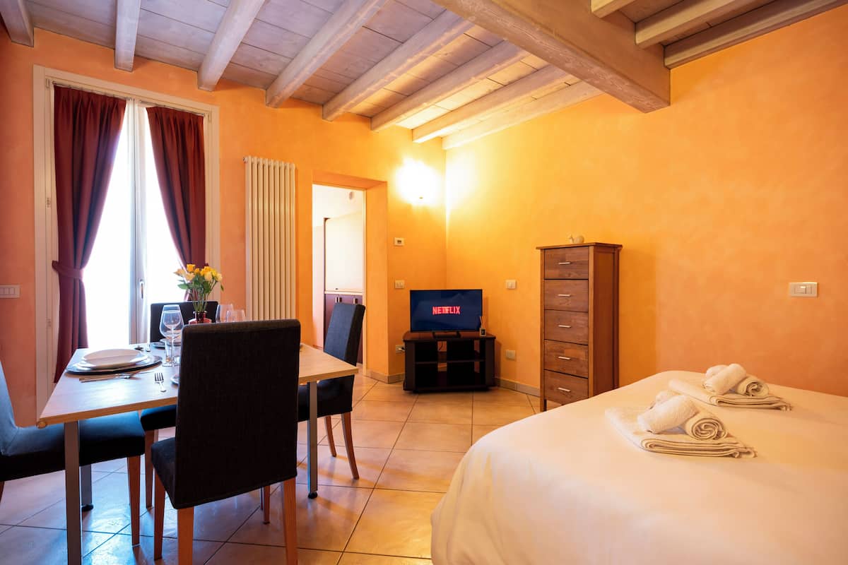 A hotel room with a bed, a TV, a dining table with chairs, and a cabinet.