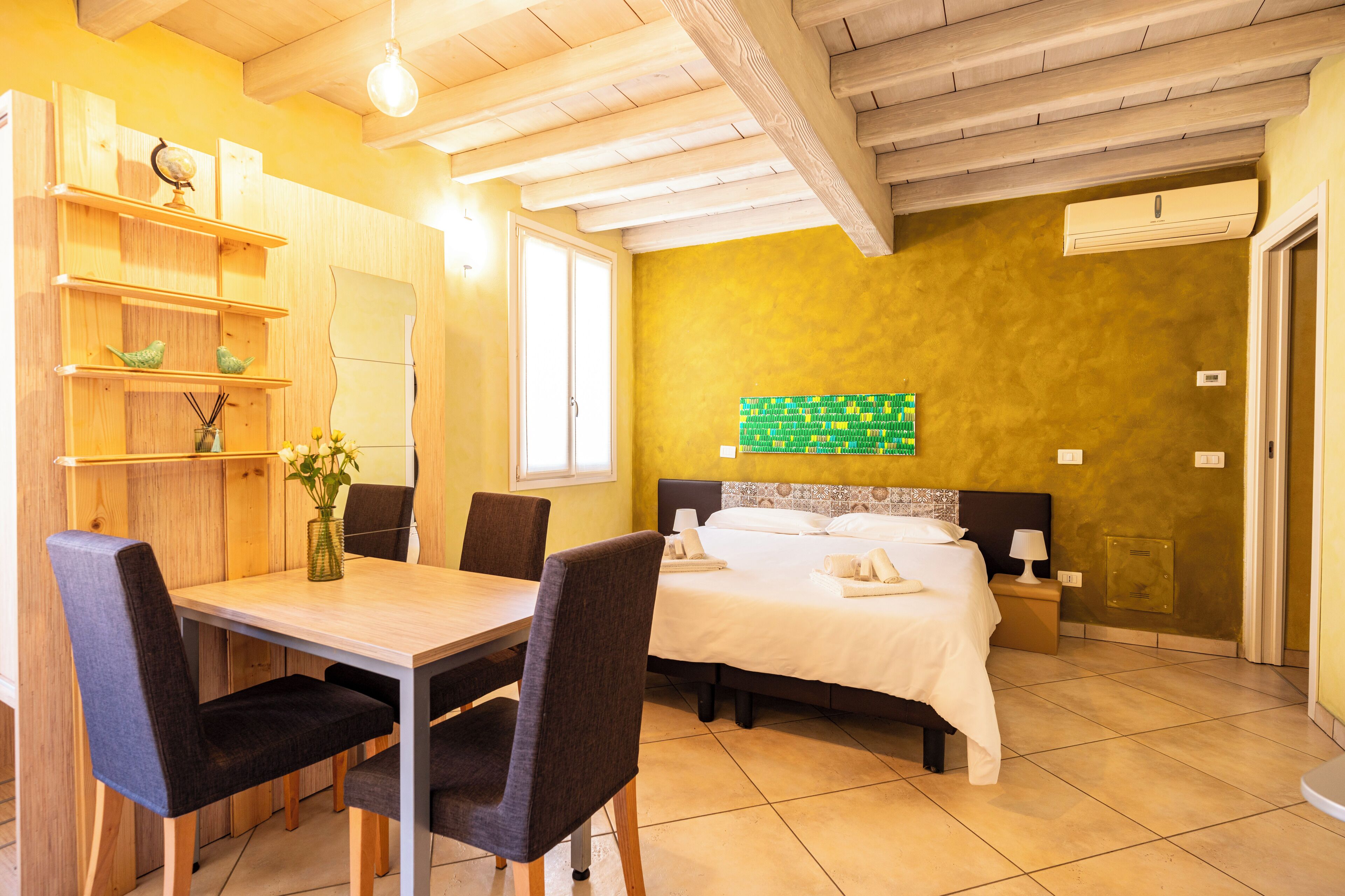 Ein Zimmer mit Bett, Nachttisch, Lampe und einem Holztisch mit Stühlen.