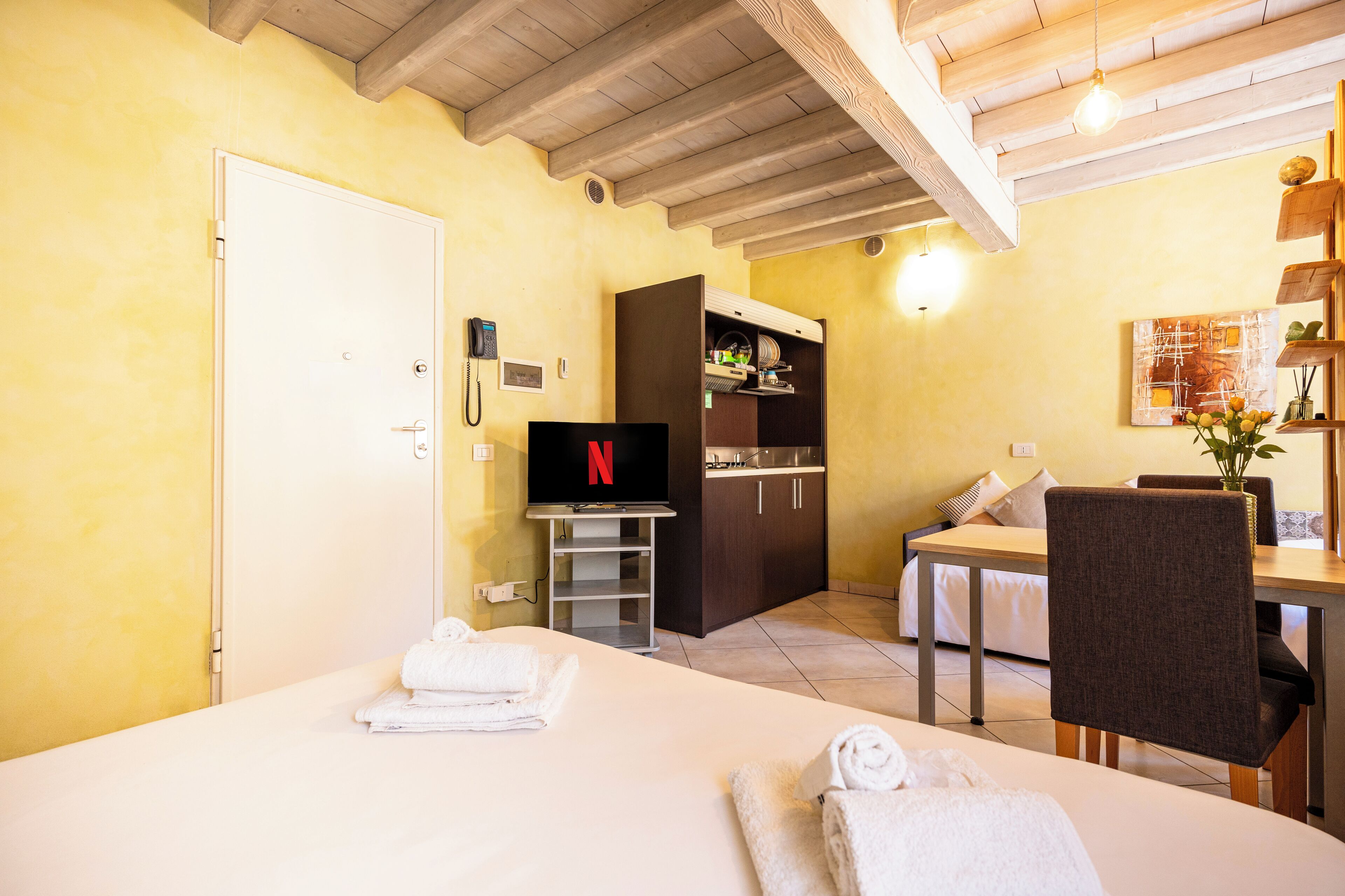 A hotel room with a bed, a TV, a desk, a chair, and a kitchenette.