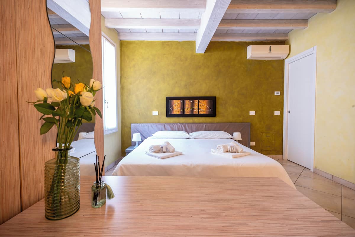 A hotel room with a bed, a vase with flowers, and a painting on the wall.