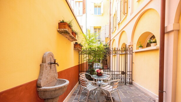 A narrow alleyway with a stone fountain, a small round table with chairs, and potted plants on the walls. - Al Podestà (Mantua)