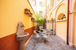 A narrow alleyway with a stone fountain, a small round table with chairs, and potted plants on the walls. - Al Podestà (Mantua)