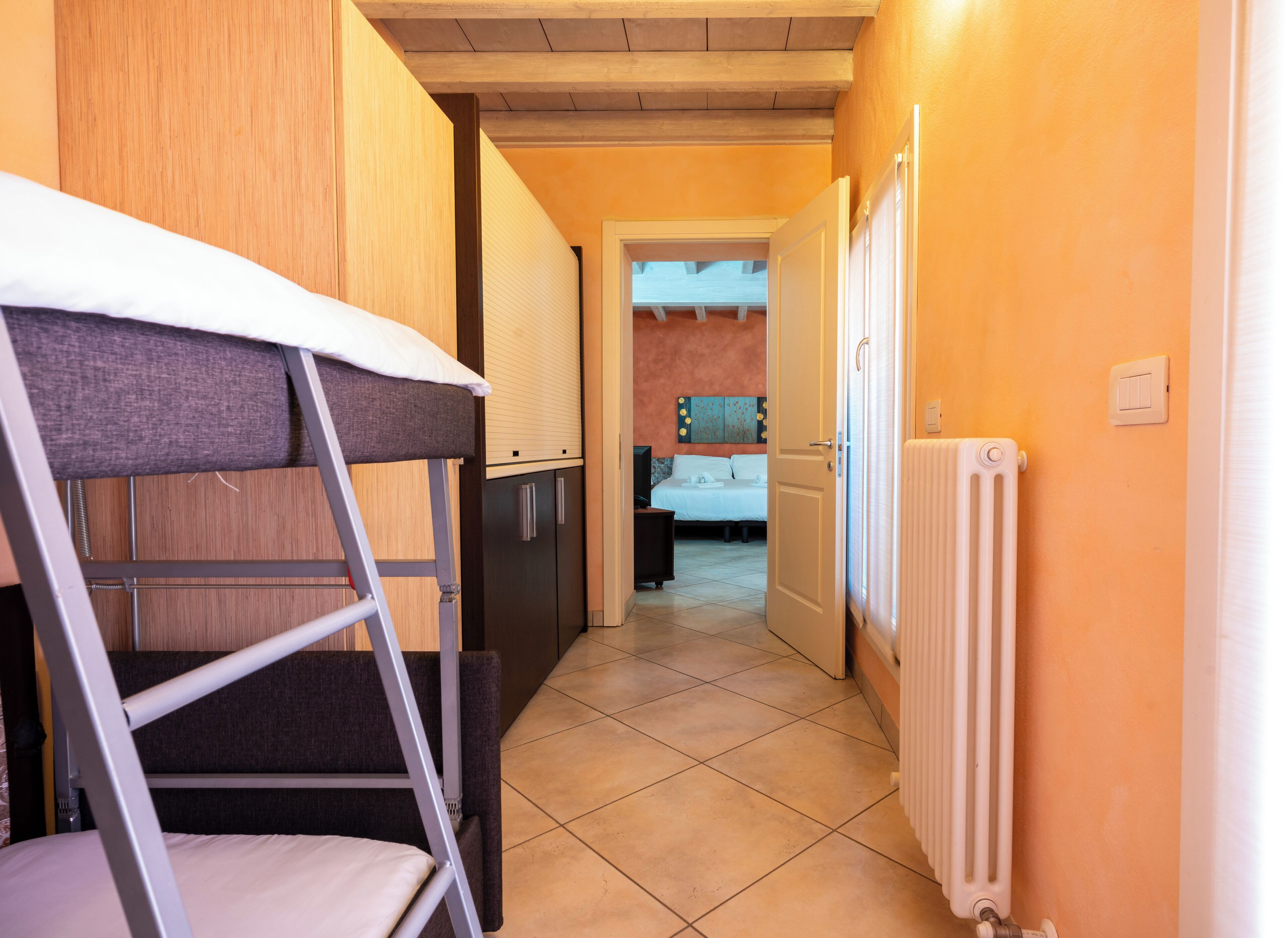 Un couloir étroit avec un lit superposé, un radiateur et un lit dans la pièce adjacente.