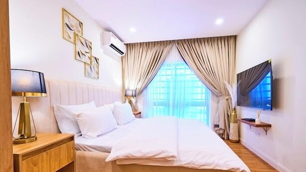A modern hotel room with a large bed, bedside lamps, a TV, and artwork on the wall. - Hillview Apartments (Abuja)