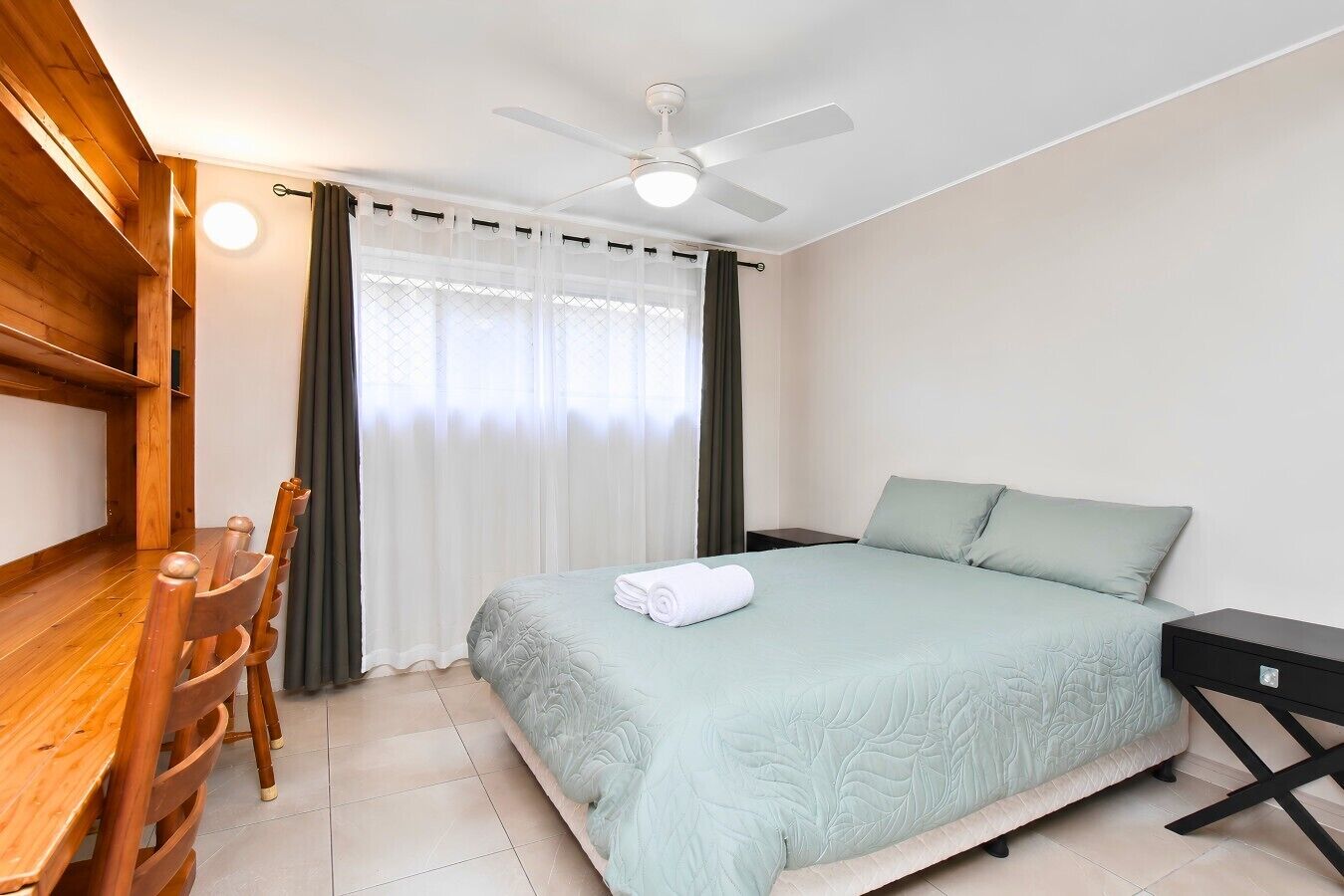 A hotel room with a bed, a desk, a chair, a nightstand, and a ceiling fan.