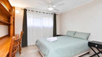 A hotel room with a bed, a desk, a chair, a nightstand, and a ceiling fan.