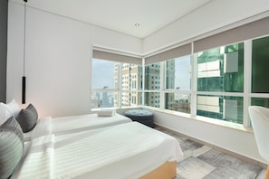 Une chambre d’hôtel moderne avec deux lits, une grande fenêtre donnant sur la ville et un petit coin salon.